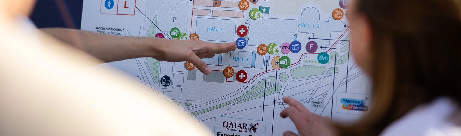 Visiteurs consultant le plan du Salon International de l’Aéronautique et de l’Espace pour s’orienter entre les halls et les services.