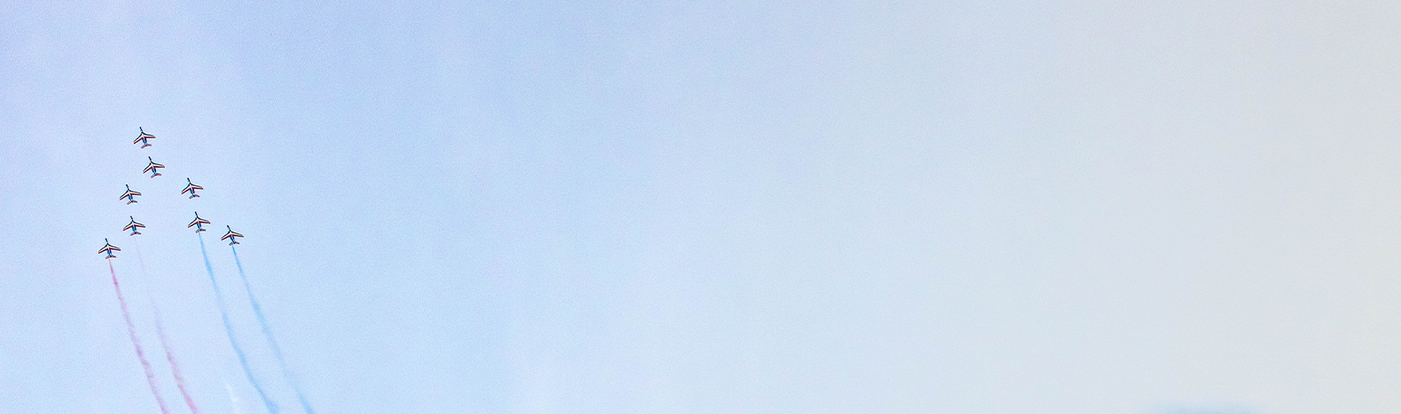 Formation de la Patrouille de France laissant des traînées de fumée colorée dans le ciel.